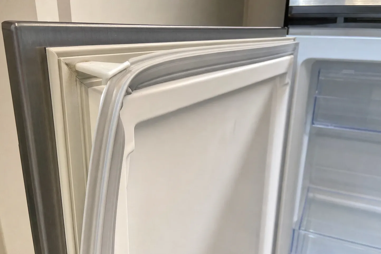 Close-up of the flexible door gasket at the top corner of an open refrigerator door, interior shelves behind